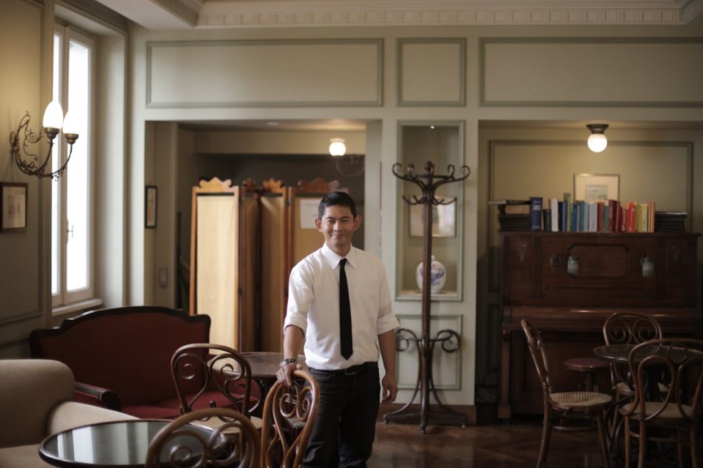 Smiling waiter stands in an elegant restaurant interior, exuding warmth and professionalism.